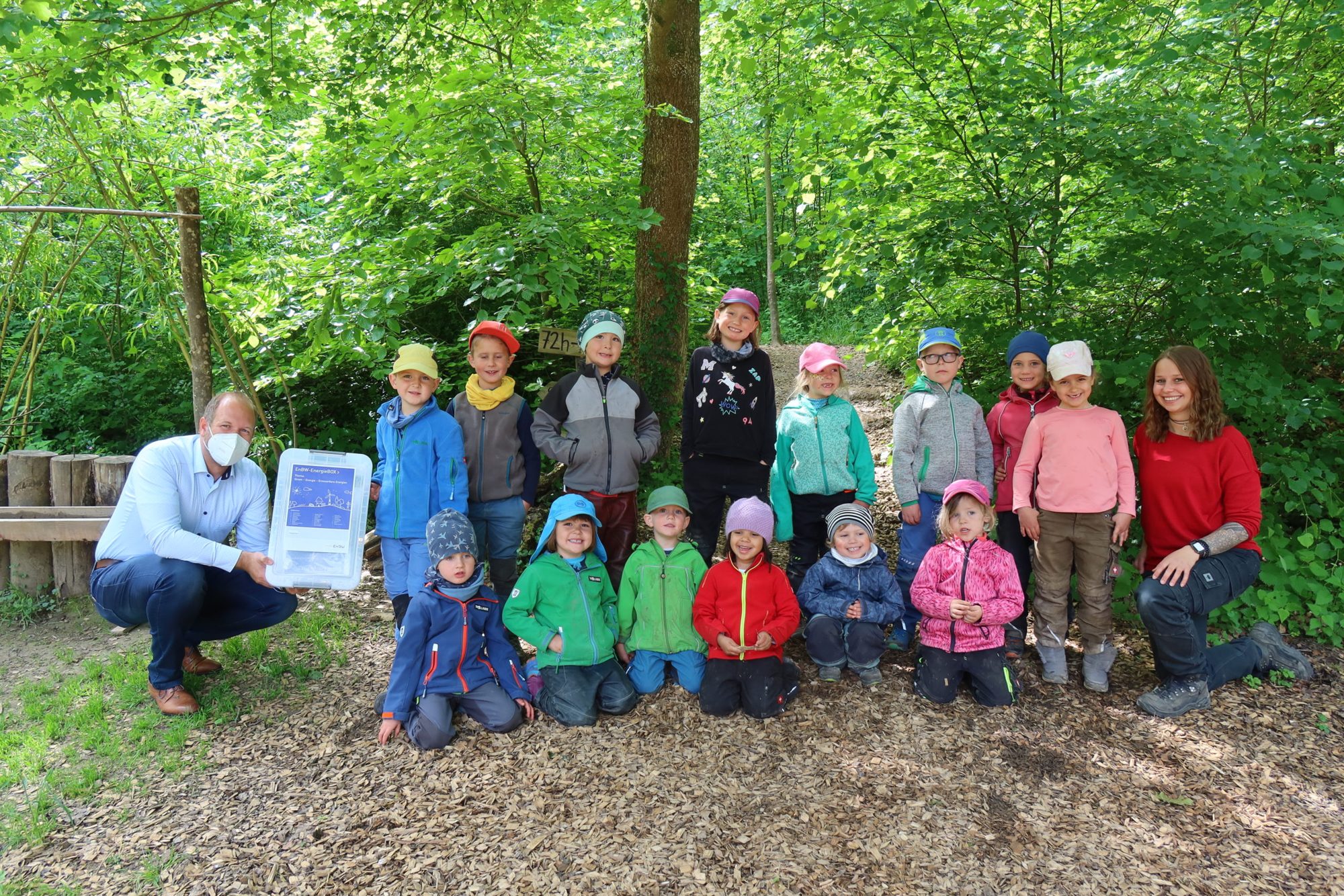 Kindergruppe mit Erzieherin und einem Besucher mit Box im Wald