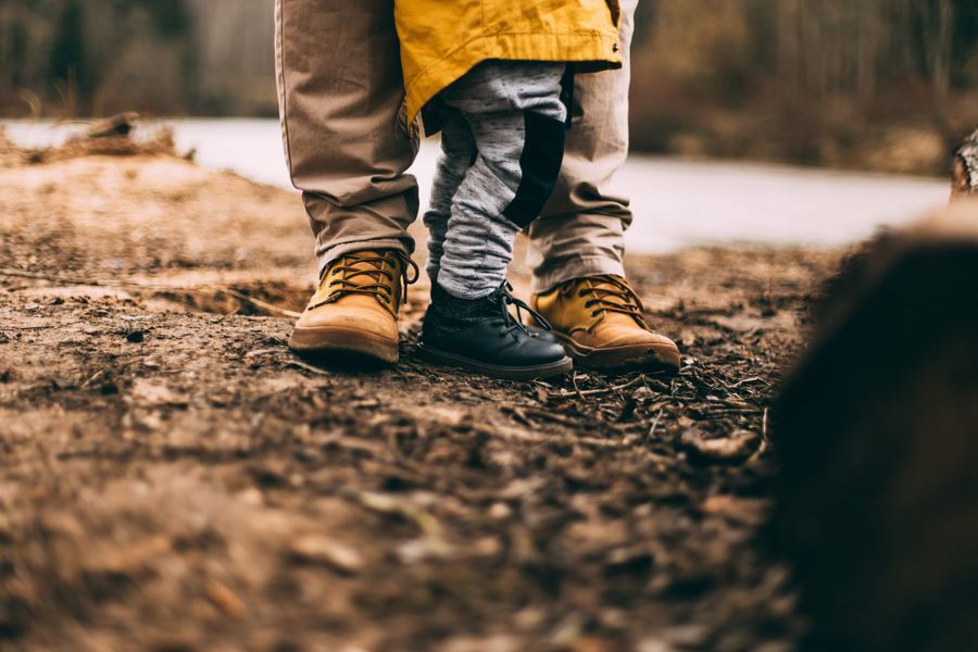 Füße eines Erwachsenen in Wanderschuhen und eines Kleinkinds auf Waldboden