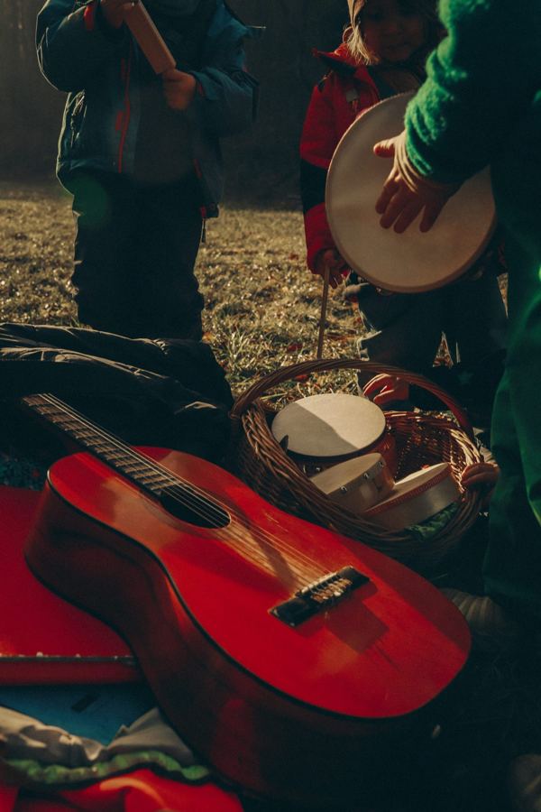 Rote Gitarre und Korb mit Trommeln, dahinter Kinder mit Instrumenten