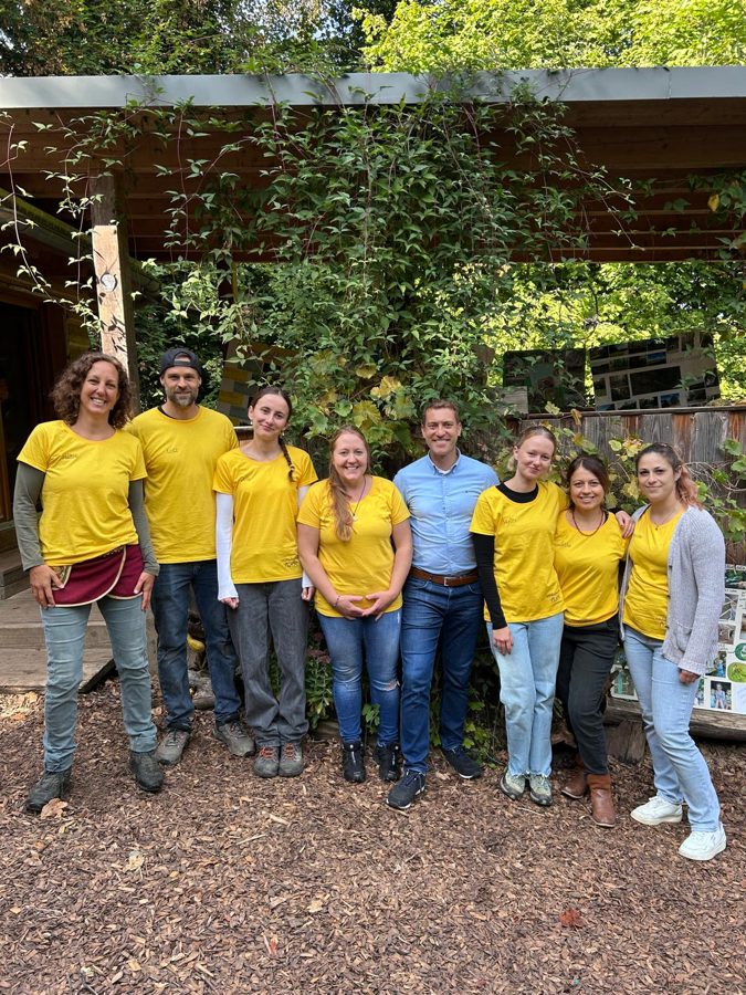 Das Team der Wurzelkinder in gelben T-Shirts mit Bürgermeister Tobias Metz am Waldkindergarten